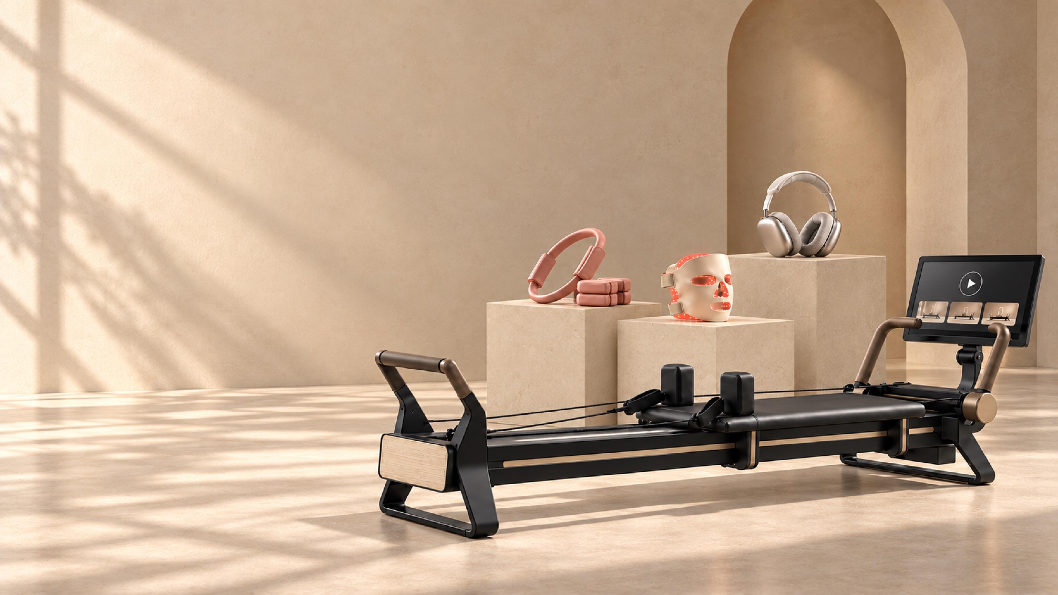 A NordicTrack reformer, AirPods Max, an Omnilux LED mask, and a Bala pilates ring on plinths in a sunlit studio