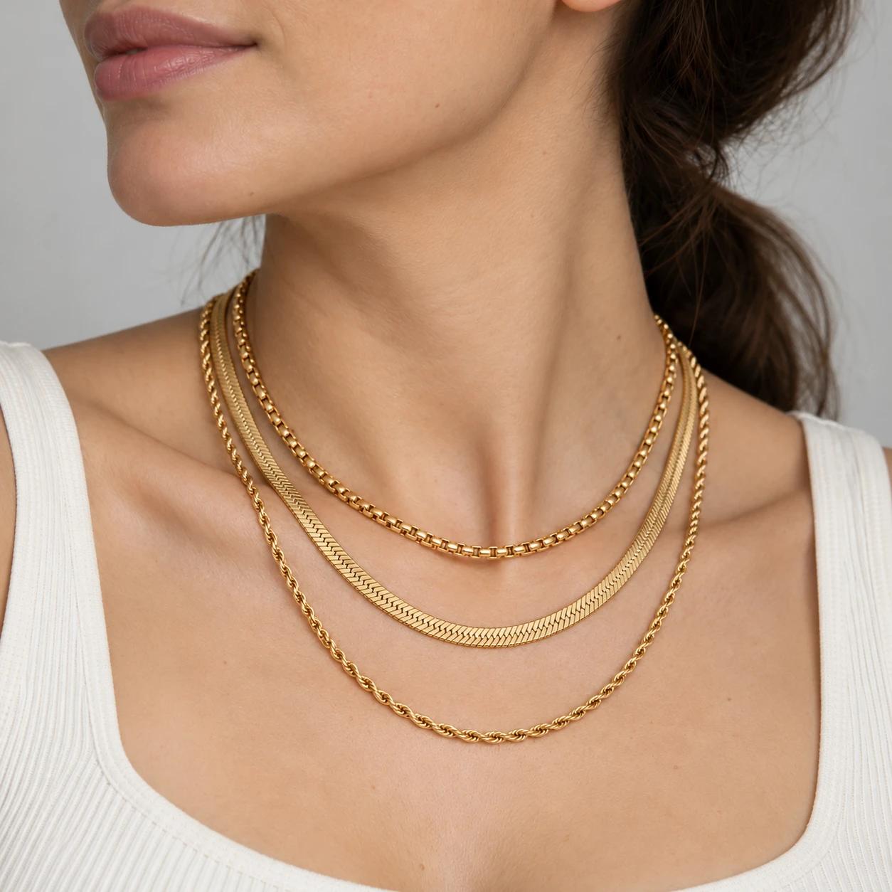 Three gold necklaces layered at distinct lengths: Box Chain, Herringbone Chain, and Rope Chain.