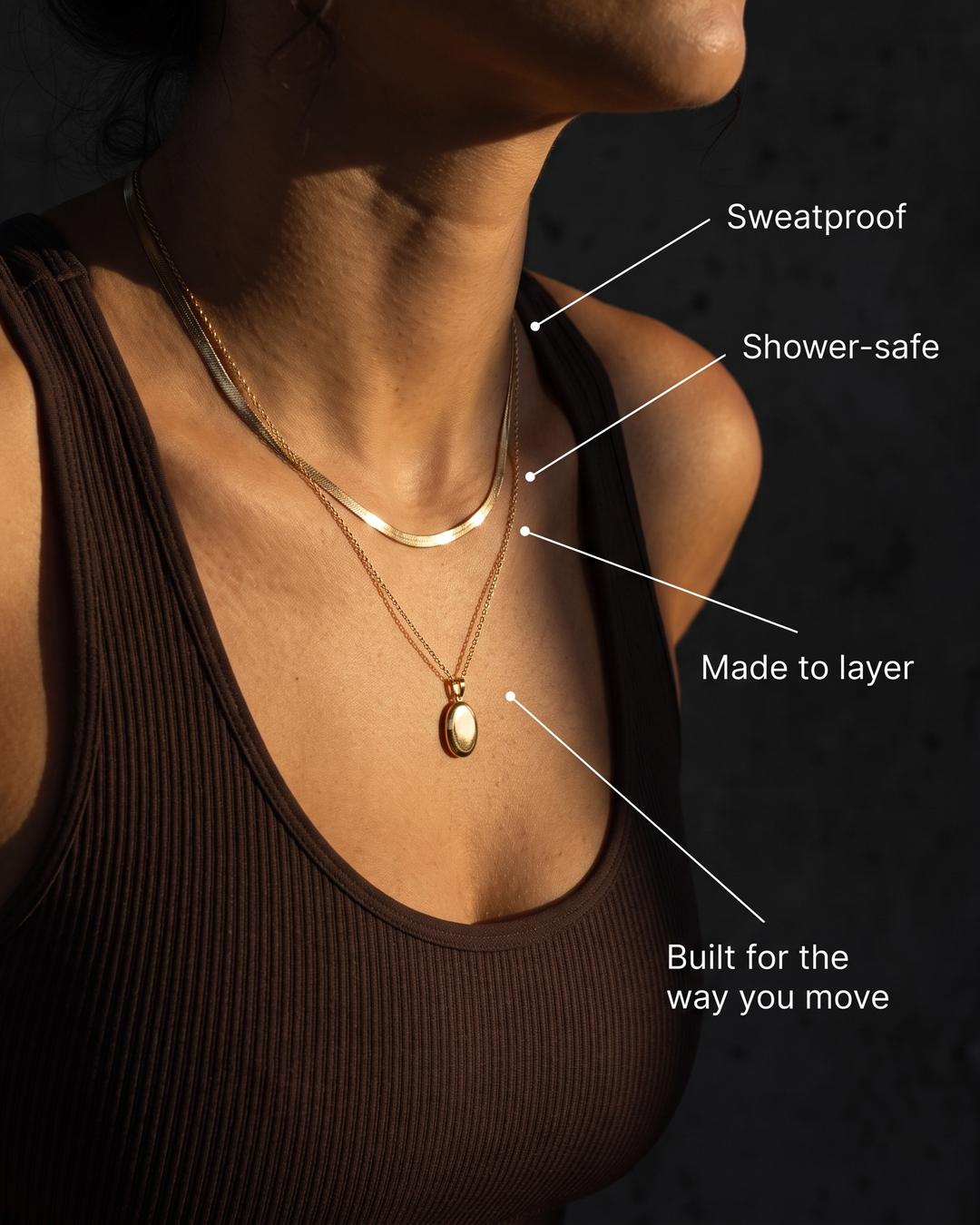 Layered gold herringbone and pendant necklace in warm sunlight.