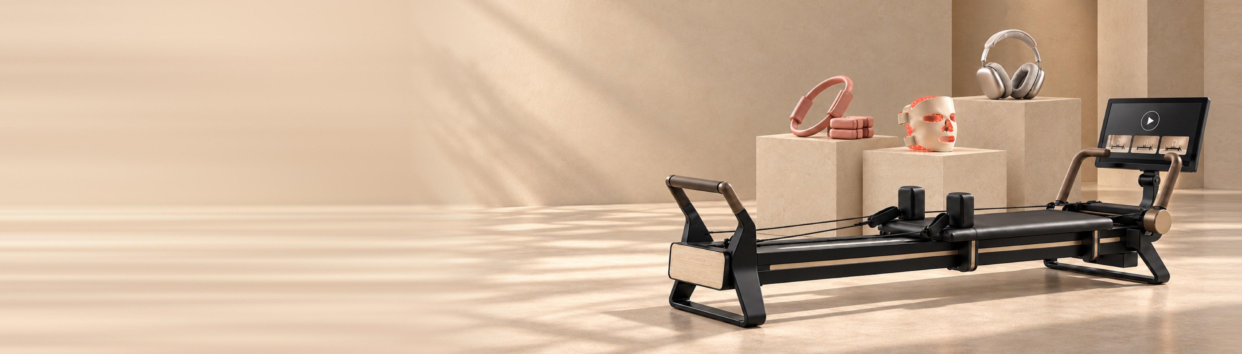 A NordicTrack reformer, AirPods Max, an Omnilux LED mask, and a Bala pilates ring on plinths in a sunlit studio