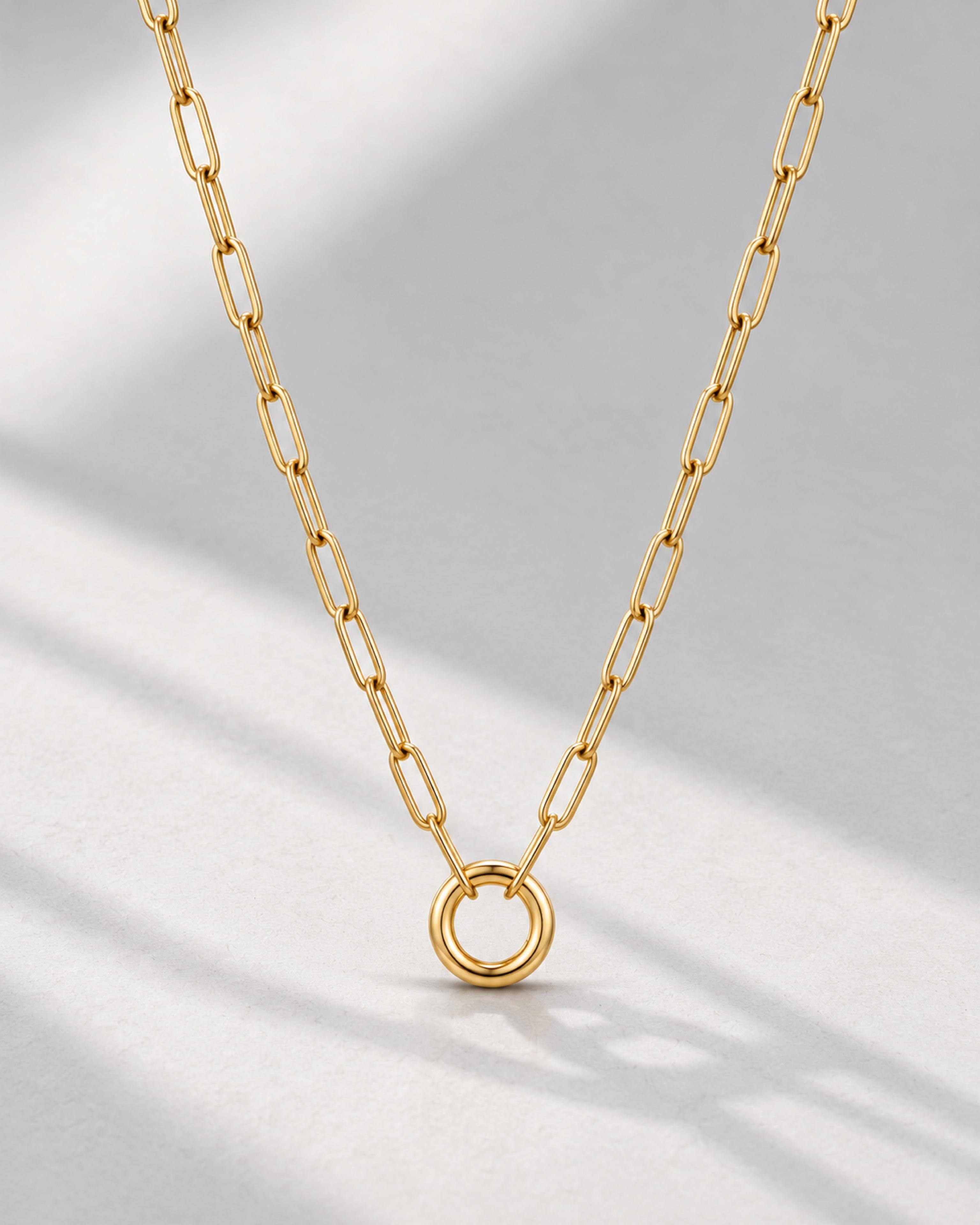 Gold paperclip charm necklace on a pale gray background