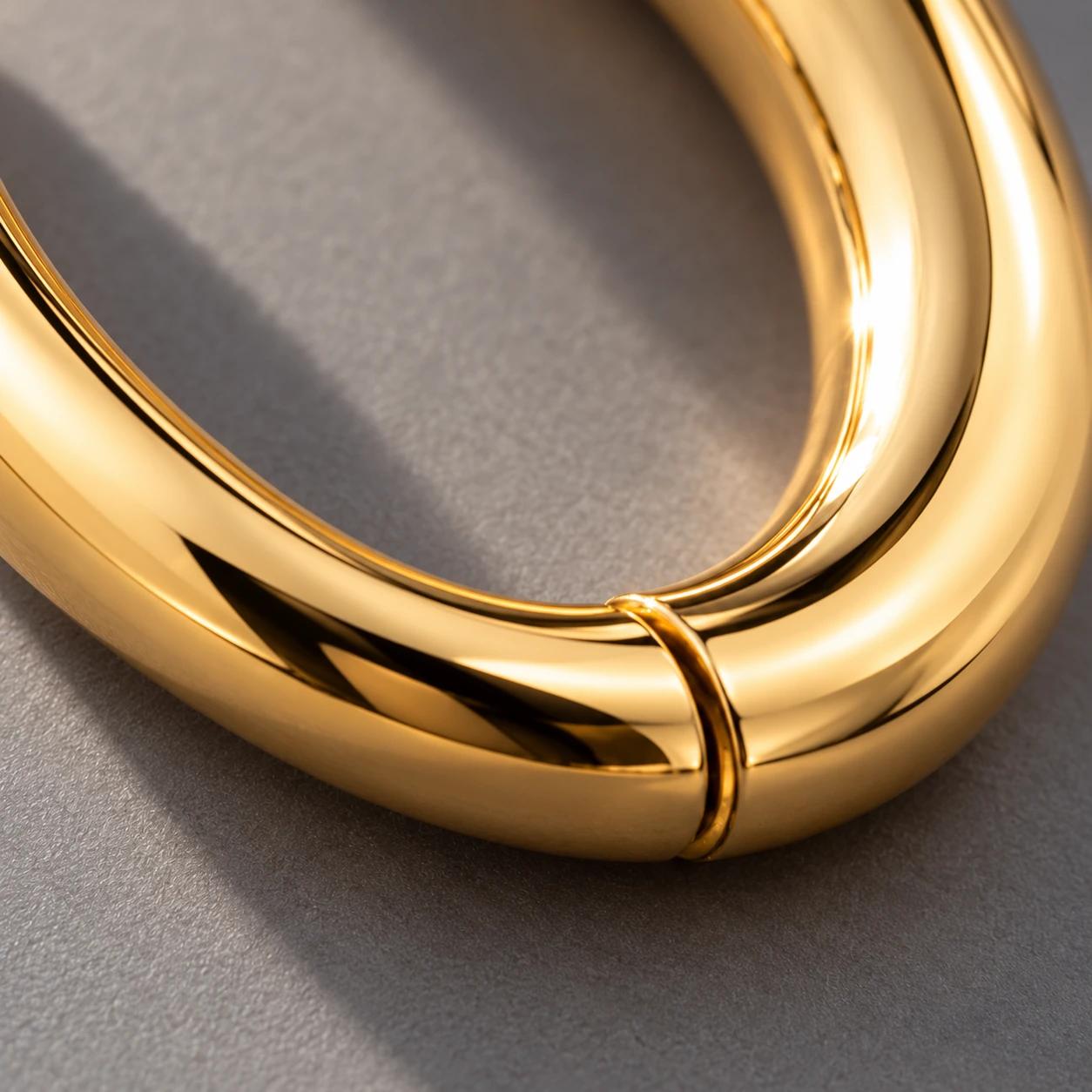 An extreme close-up of the smooth gold curve and hinge of a Lune huggie hoop