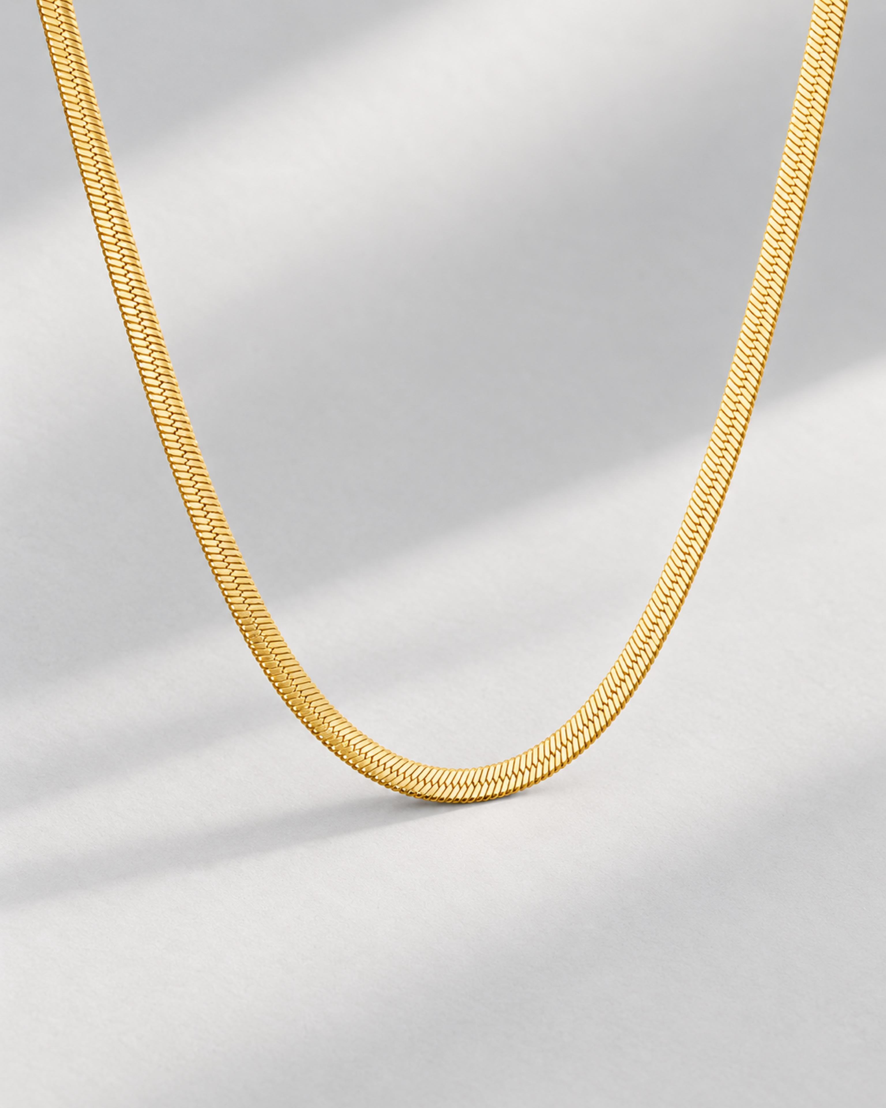 Gold herringbone necklace on a pale gray background