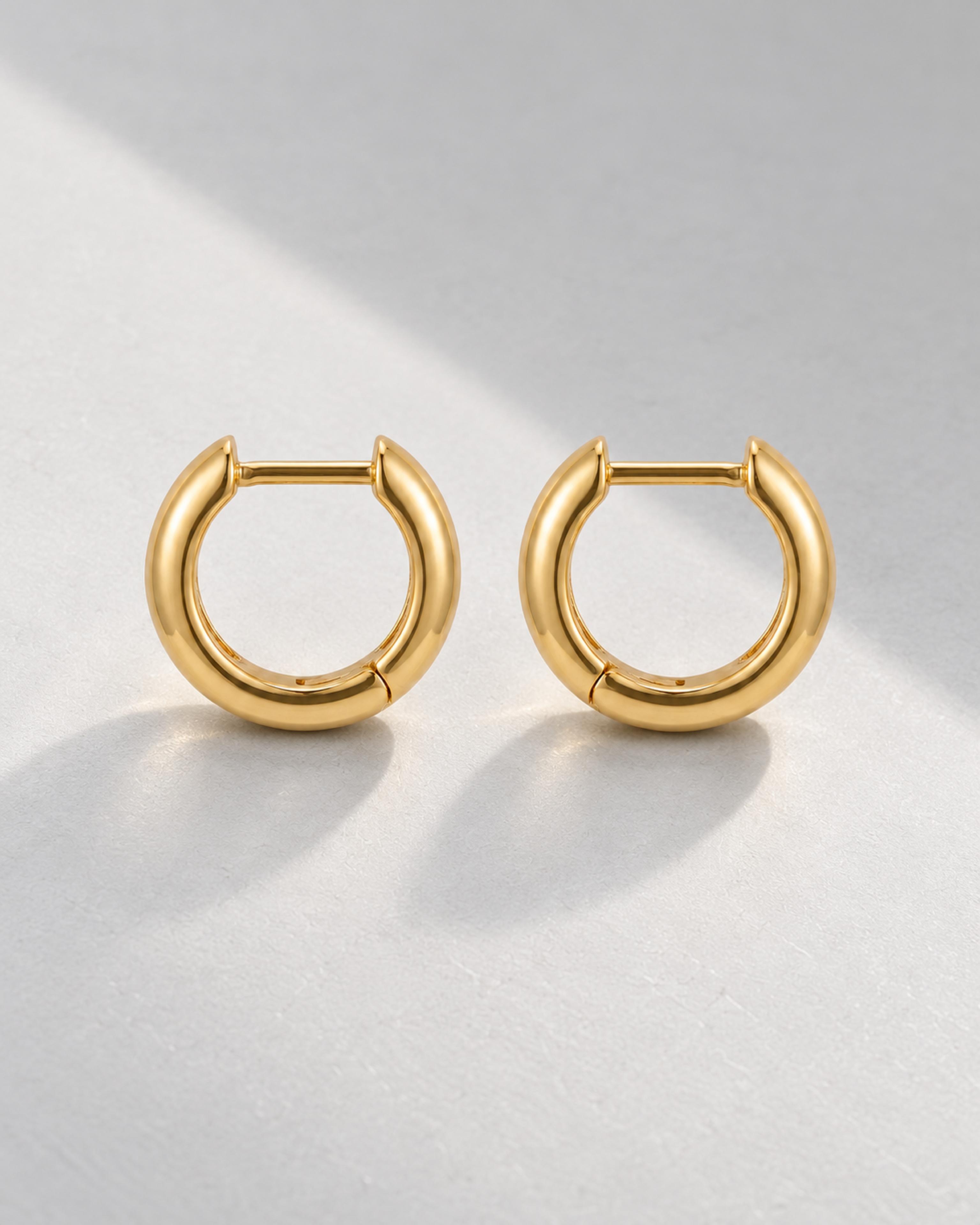 Pair of gold huggie hoops on a pale gray background