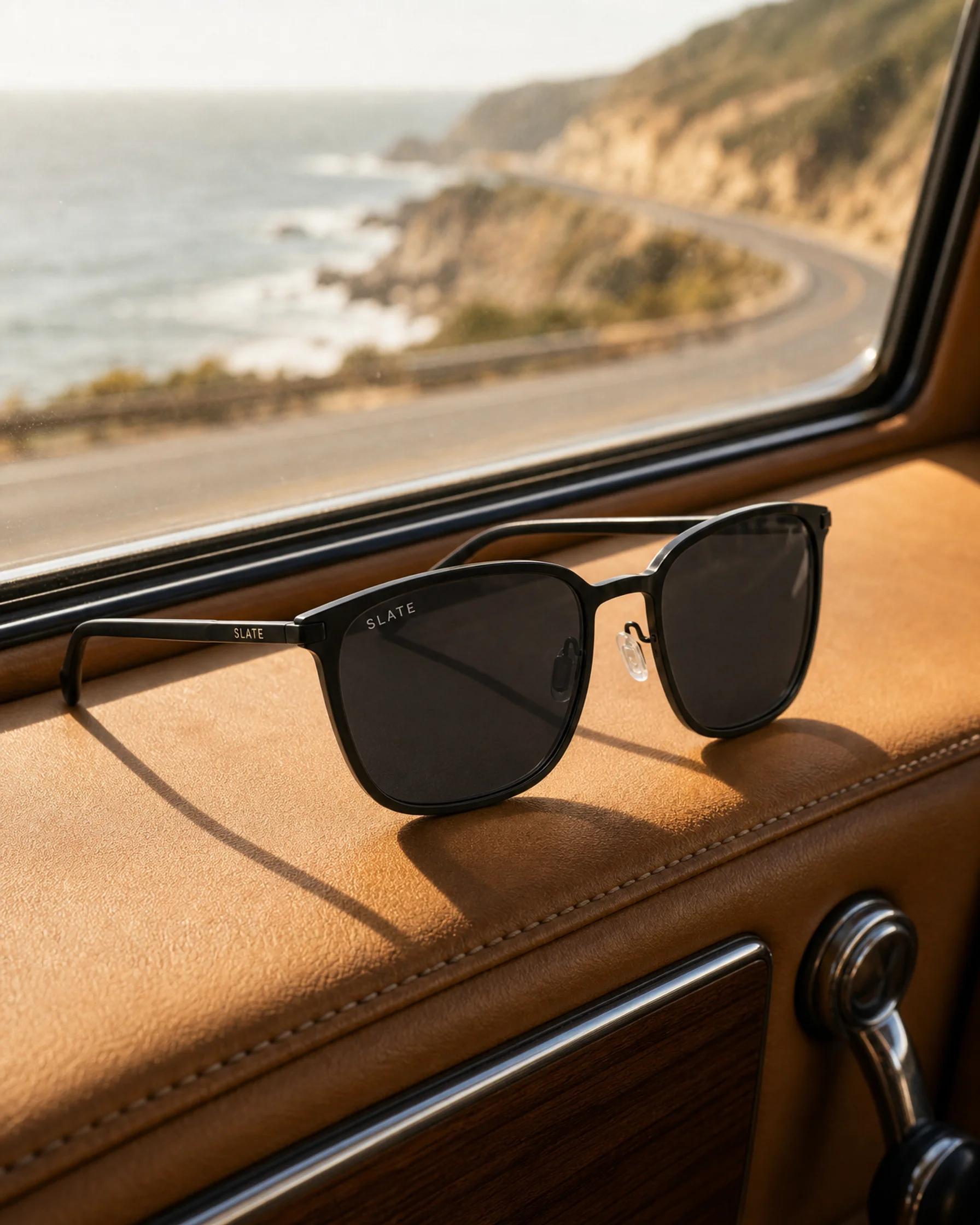 Slate Ledge sunglasses resting on a car dashboard with a coastal highway ahead